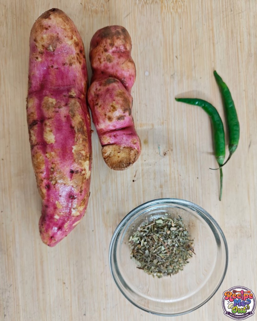 Flat lay image showing the key ingredients: a whole sweet potato, a bowl of shredded melting cheese, fresh green chilies, and a small dish of mixed dried herbs (rosemary, basil, oregano).
