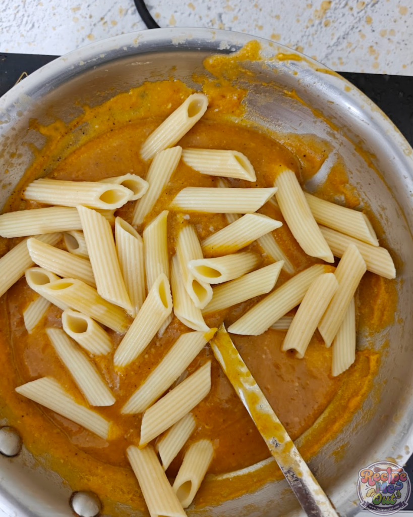 Partially cooked penne pasta added to the pumpkin sauce in the pan.
