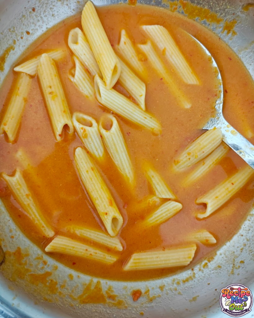 Penne pasta simmering in tomato mustard sauce and absorbing flavors