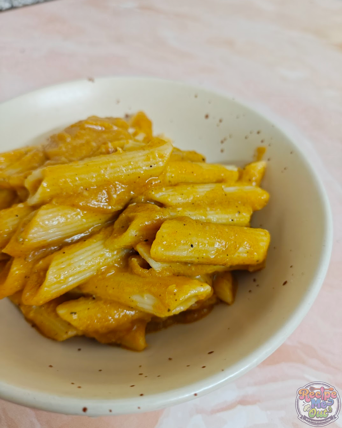 Close-up view of penne pasta coated in pumpkin sauce with visible seasoning.
