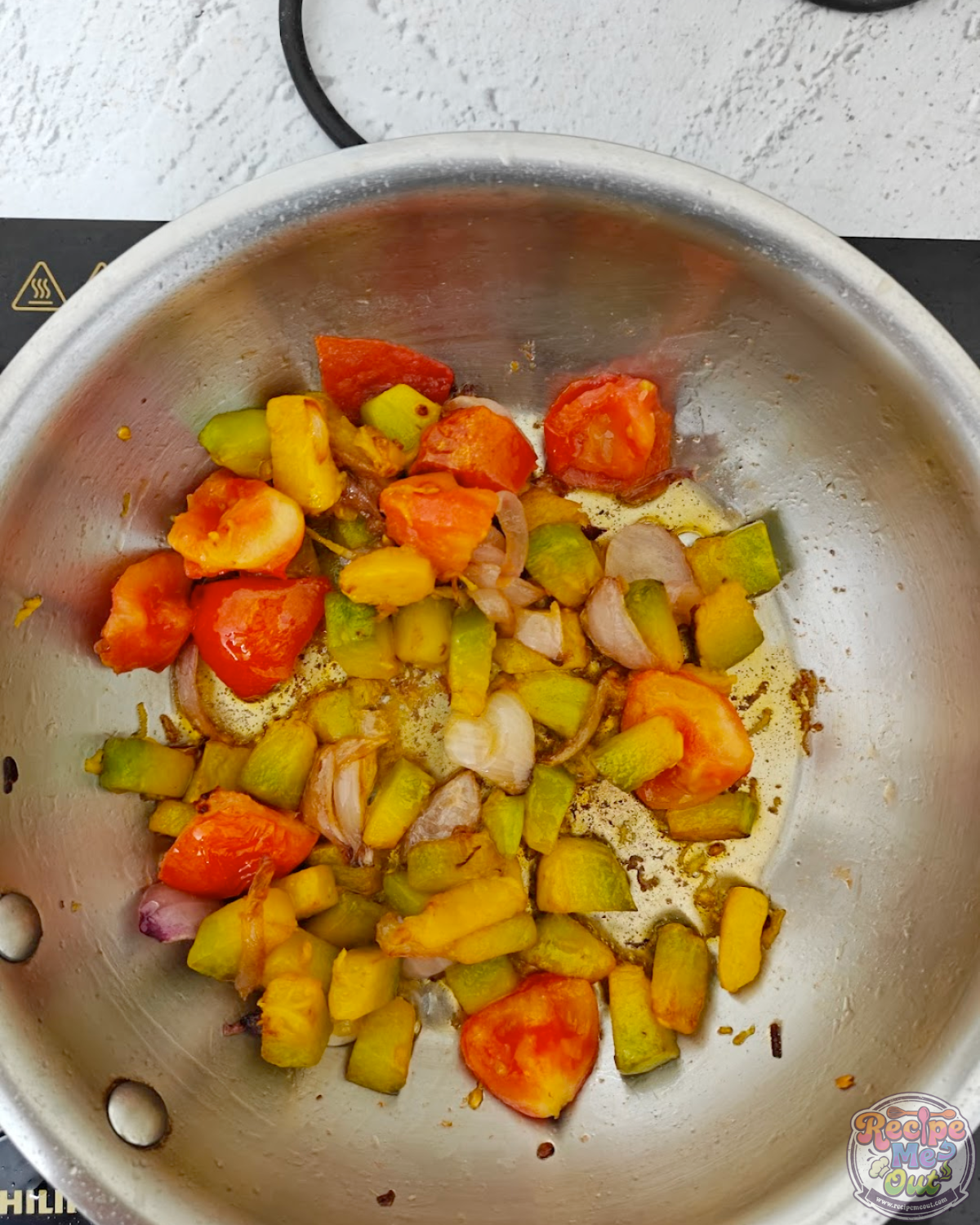 Cooked pumpkin, tomatoes, onions, and green chillies softening together in a pan.
