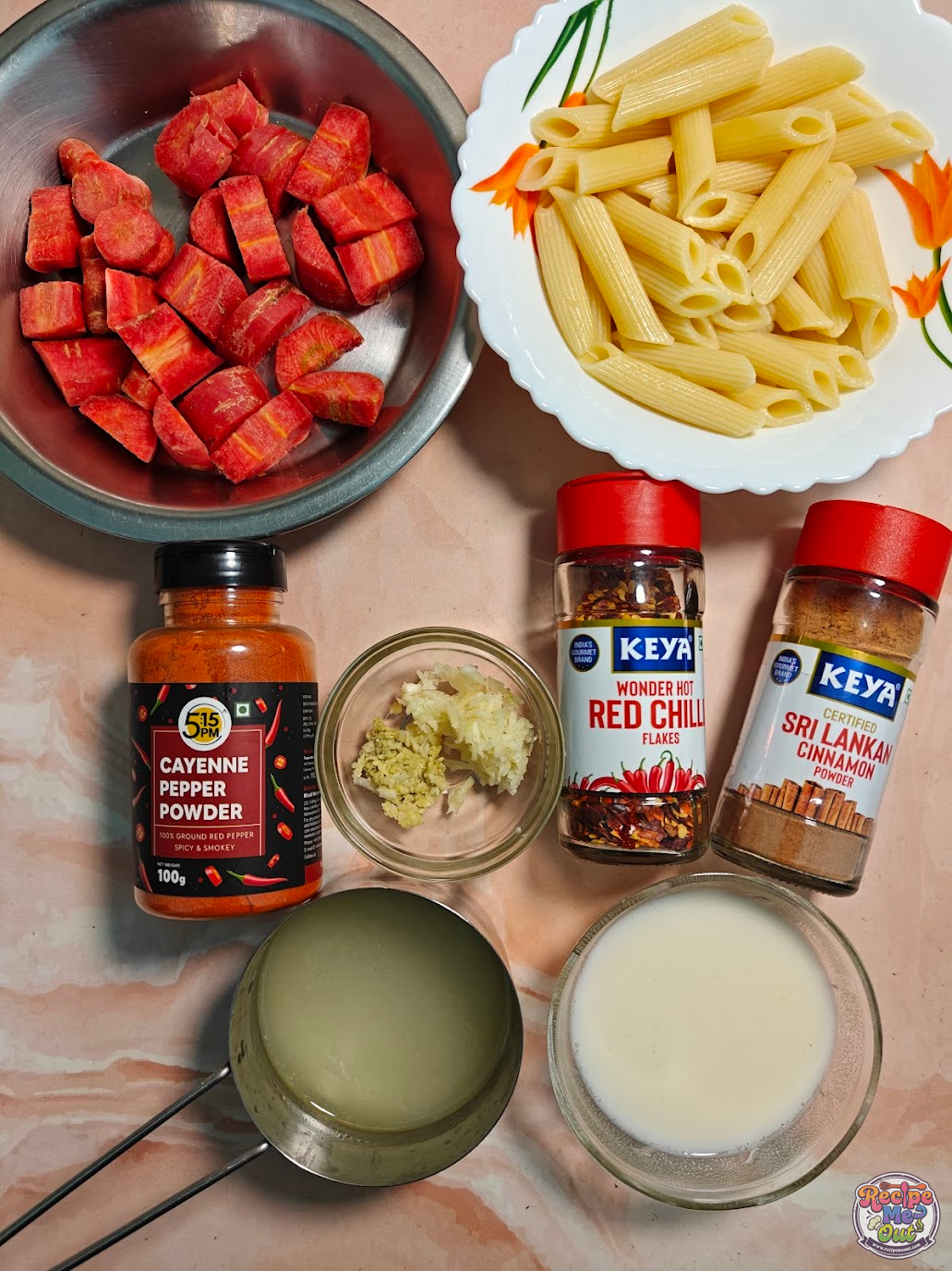 Ingredients for carrot sauce pasta including chopped carrots, penne pasta, cayenne pepper powder, red chilli flakes, cinnamon powder, grated ginger, grated garlic, milk, and reserved pasta water arranged on a counter.