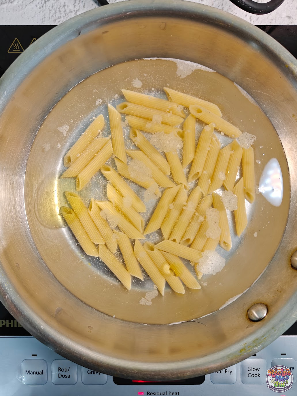 Penne pasta boiling in salted water in a stainless steel pan during the first step of making carrot sauce pasta.