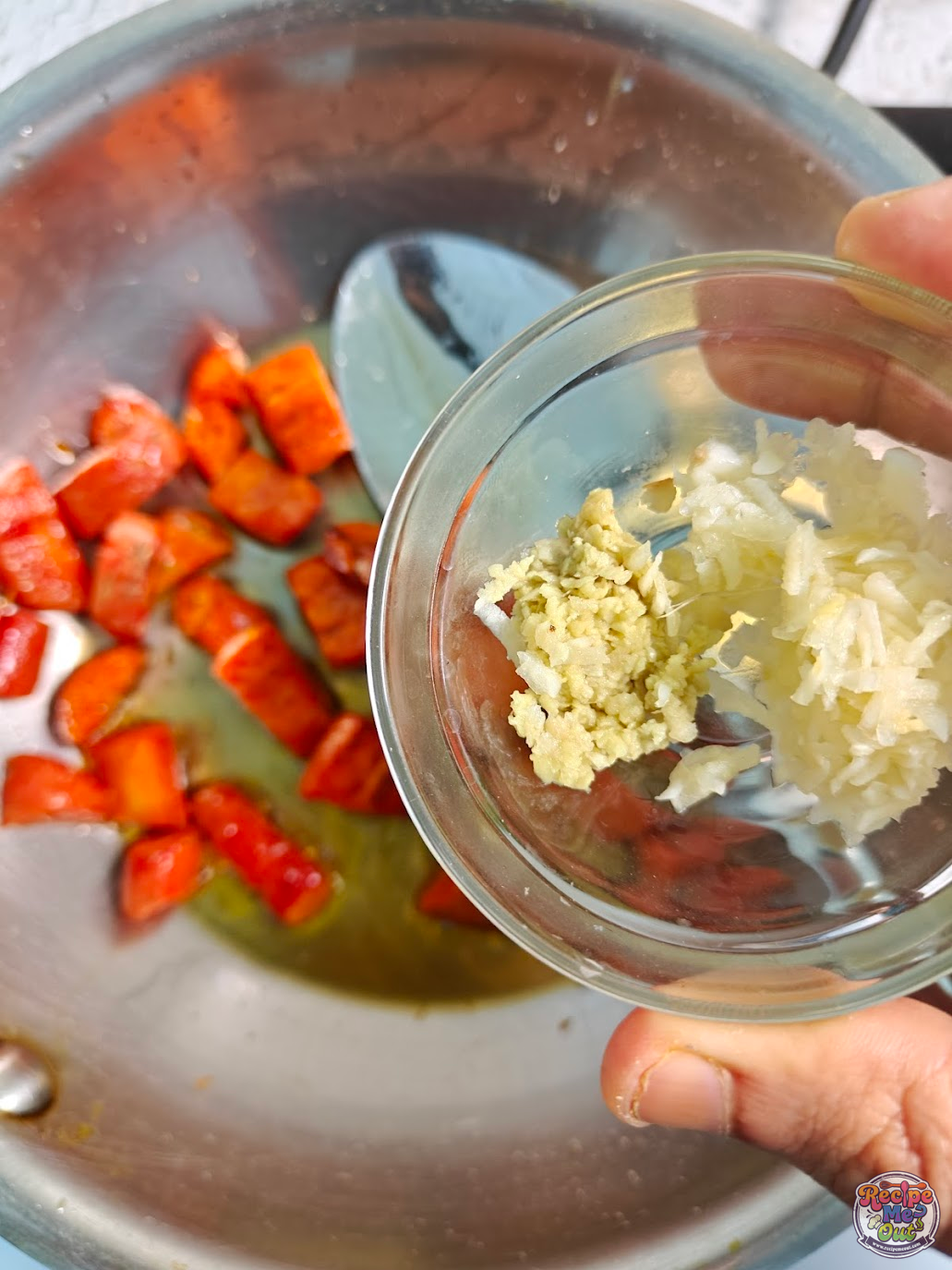 Grated ginger and garlic being added to sautéed carrots in a pan and cooked together on low heat for the carrot sauce.