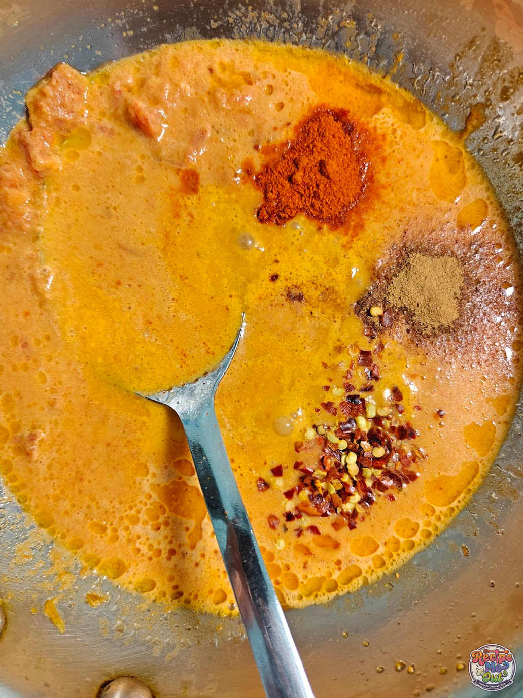 Spices including cayenne pepper, red chilli flakes, and cinnamon powder being added to the carrot sauce
