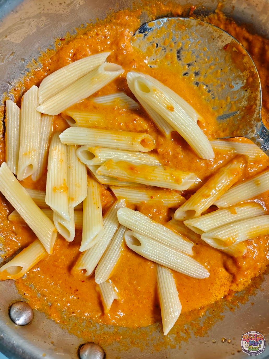 Cooked penne pasta being added to the carrot sauce 