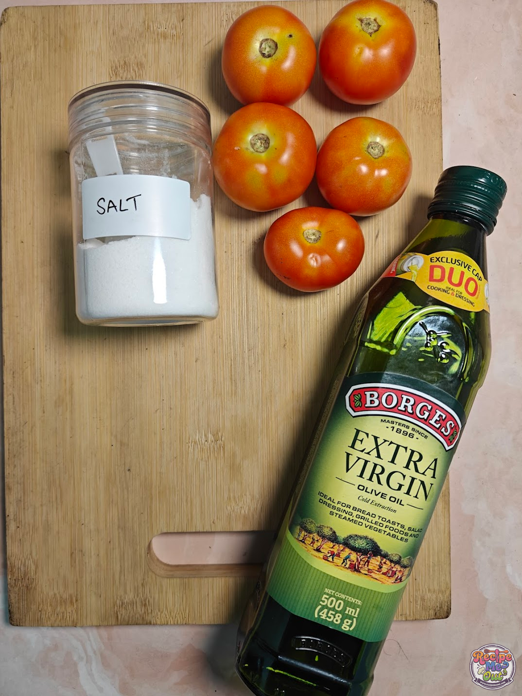 Fresh whole tomatoes, a jar of salt, and a bottle of extra virgin olive oil arranged on a wooden cutting board.
