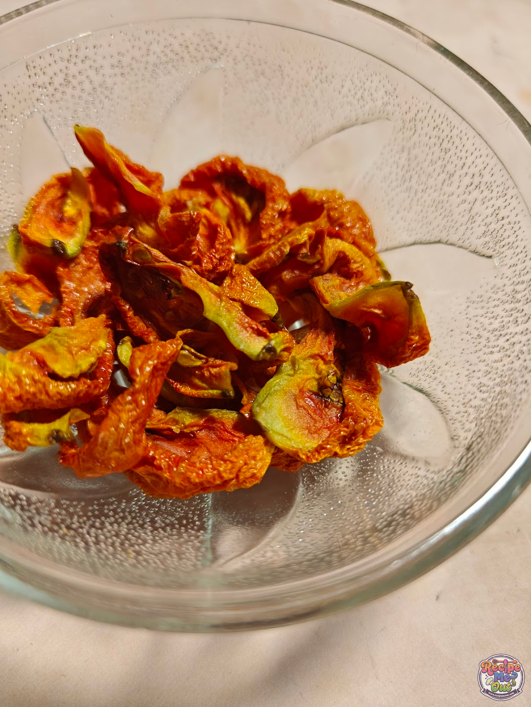 Close Up view of air fryer sun-dried tomatoes in a glass bowl, showing their wrinkled texture and concentrated color.