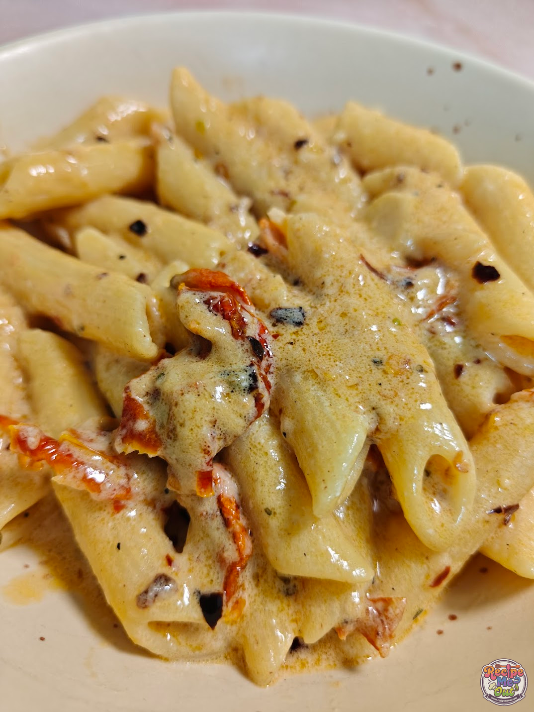 Close-up of creamy penne pasta coated in rich Parmesan sauce with herbs