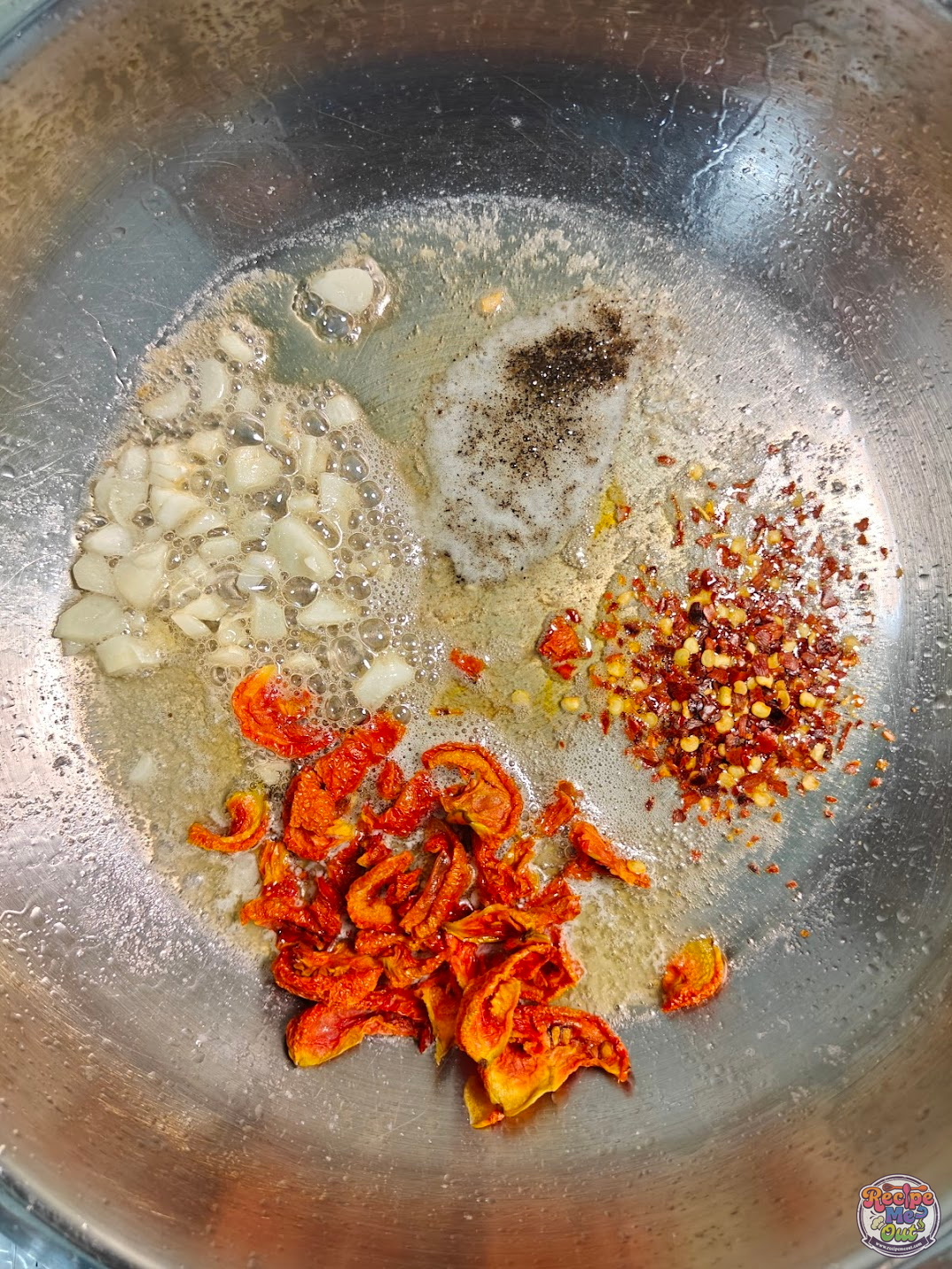 Garlic, sun-dried tomatoes, chilli flakes, and black pepper added to the pan