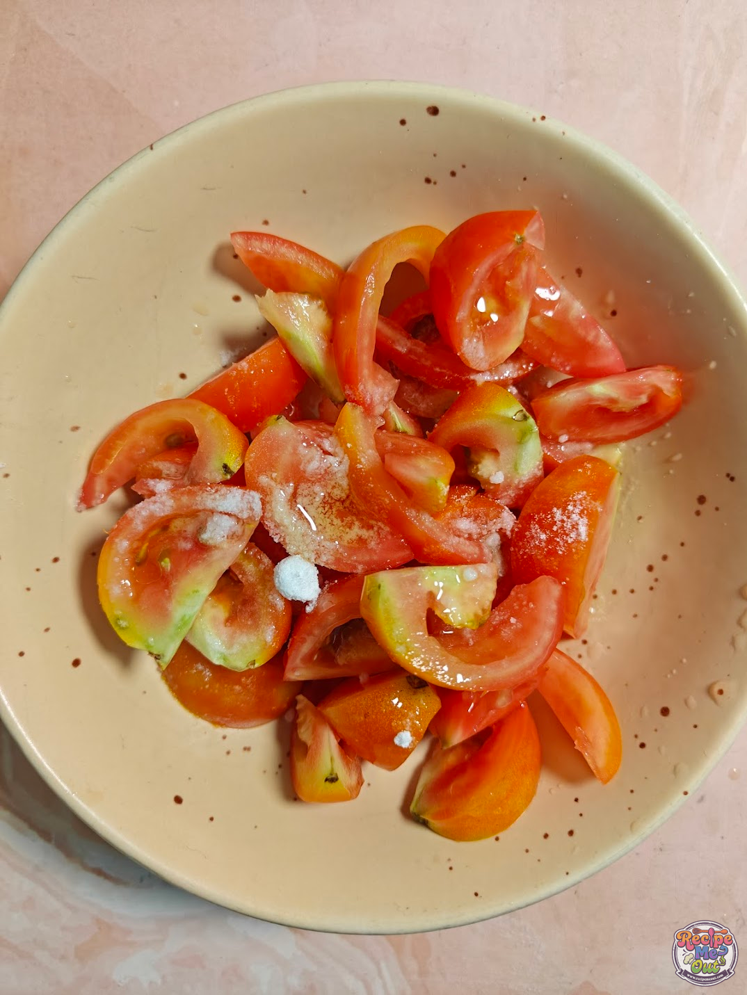 Tomato wedges in a bowl with salt sprinkled on top before mixing.