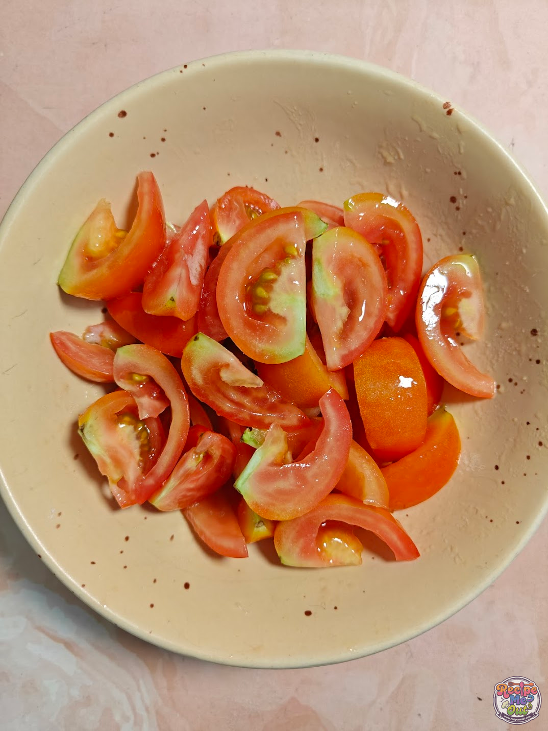Tomato wedges tossed with olive oil and salt in a bowl, evenly coated and ready for air frying.