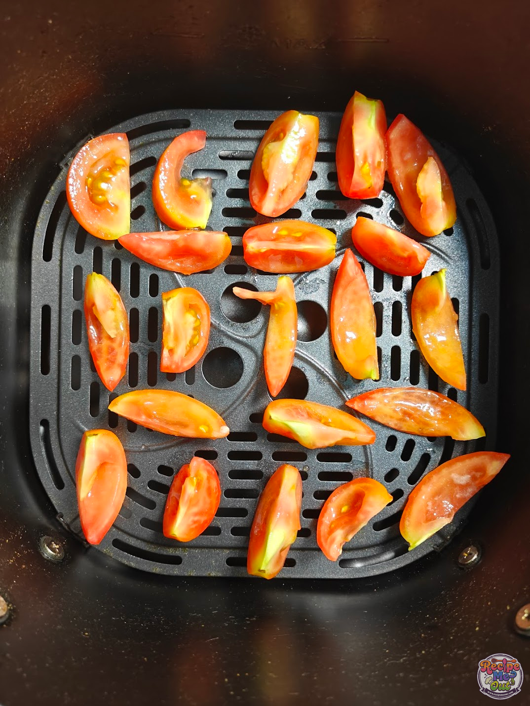 Seasoned tomato wedges arranged in a single layer inside an air fryer basket with space between pieces.