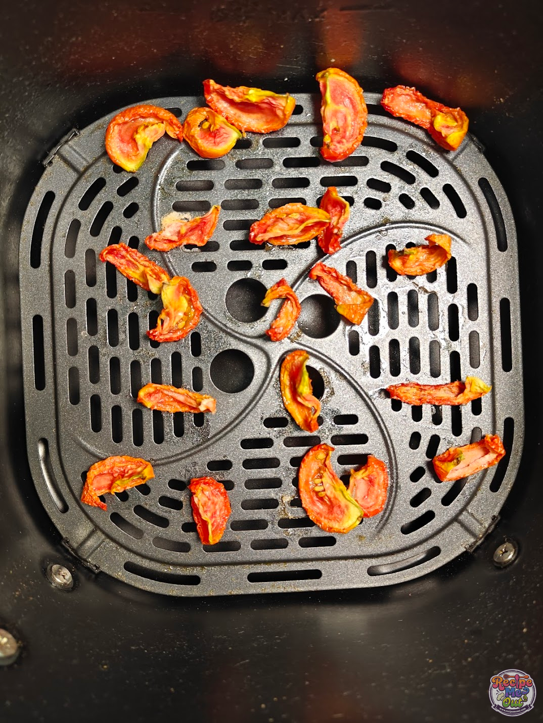 Partially dried tomato wedges inside the air fryer basket, visibly shriveled and reduced in size.
