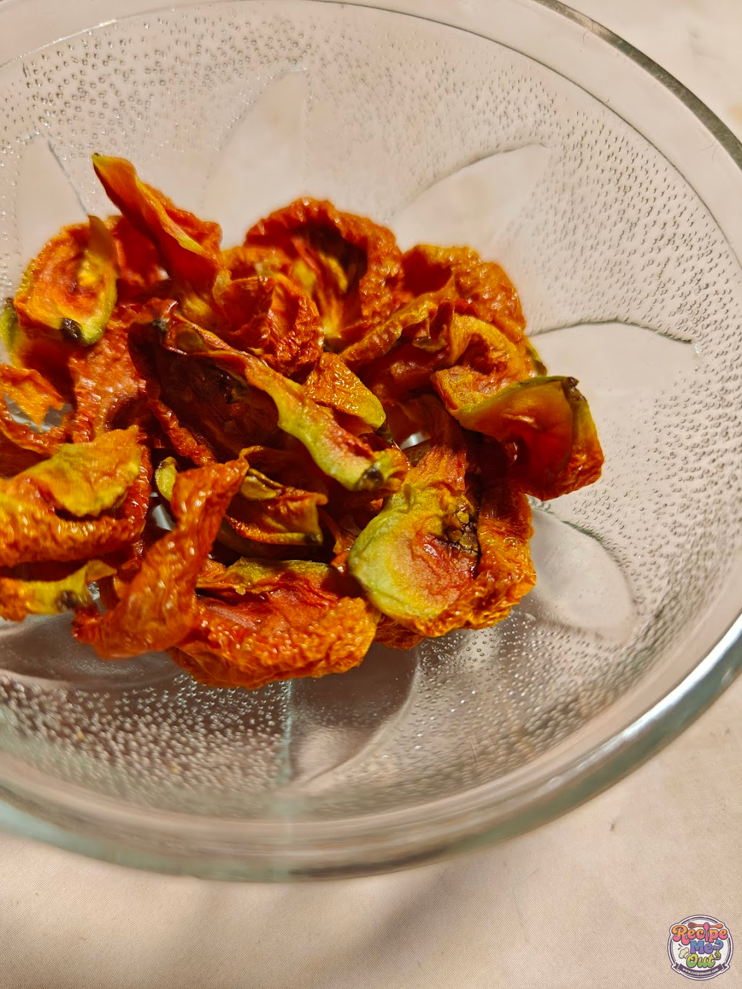 Air fryer sun-dried tomatoes in a glass bowl, showing shriveled, deep red tomato slices with slightly crisp edges.