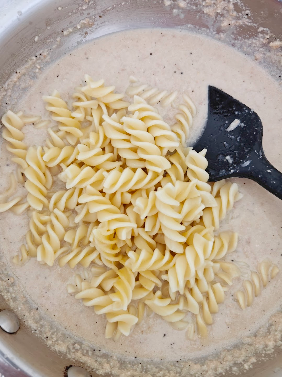 fusilli pasta being added to the paste