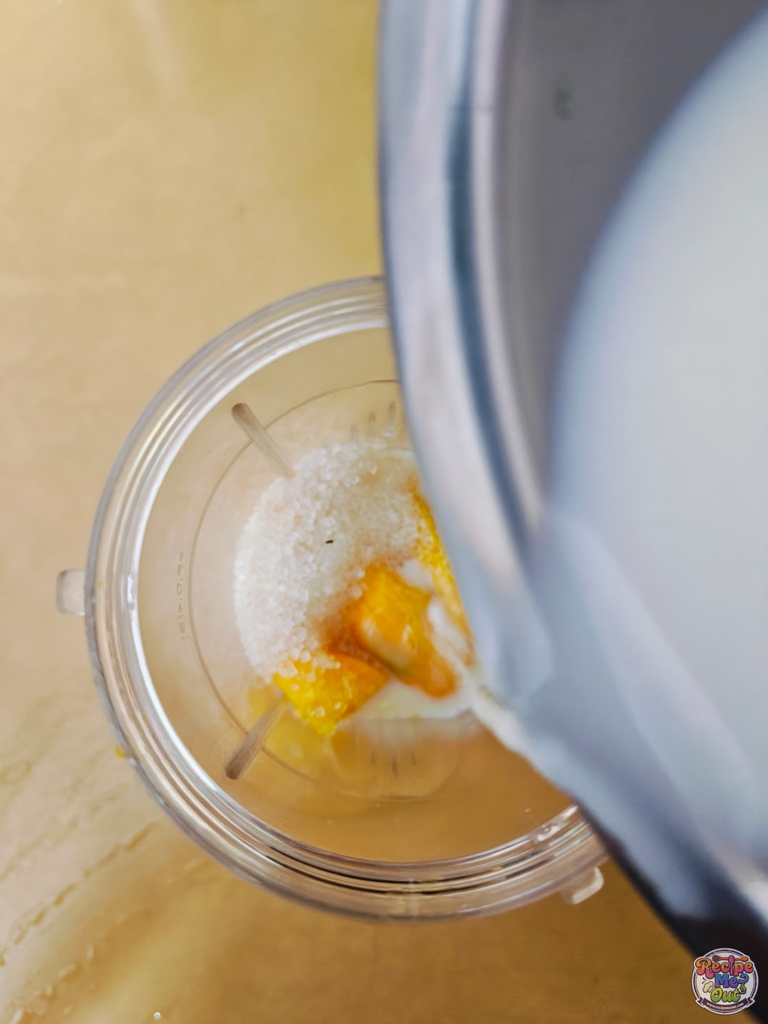 Milk being poured into the blender that already has the mangoes and the sugar