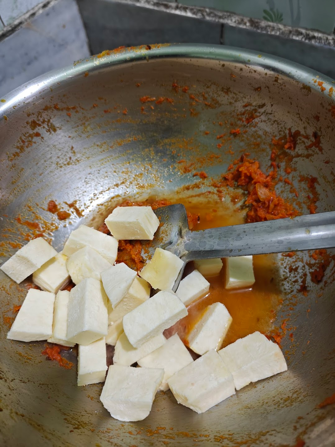 Paneer cubes being added to thick masala gravy in a pan.