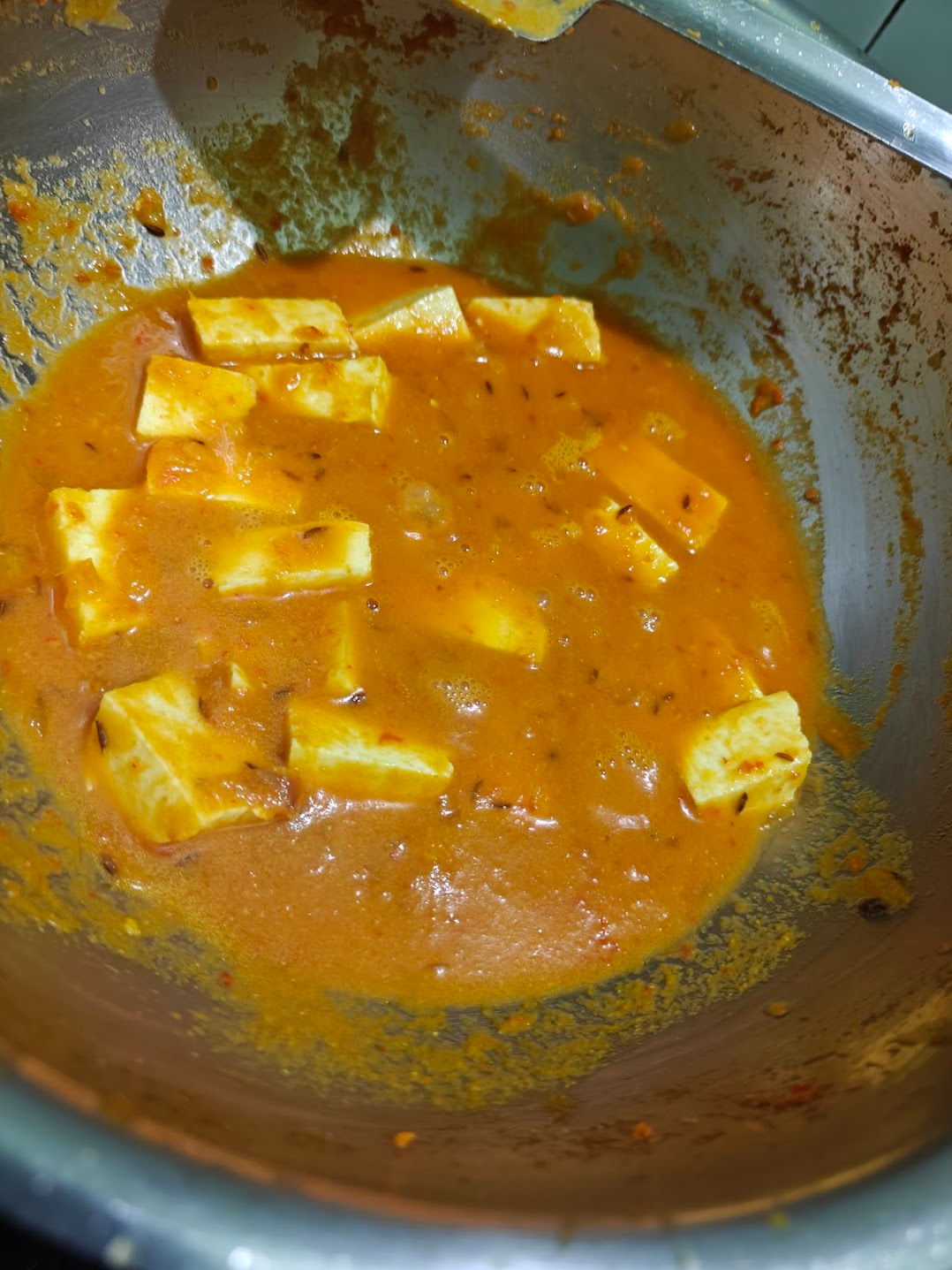 Paneer cubes cooking in spiced tomato onion gravy for paneer masala.