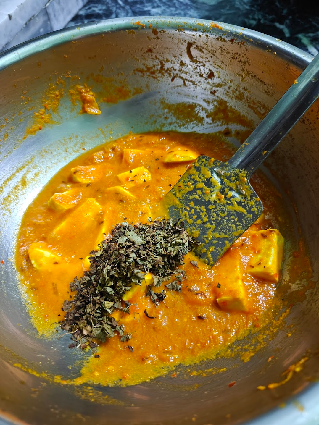 Crushed kasuri methi being added to hot paneer masala gravy.