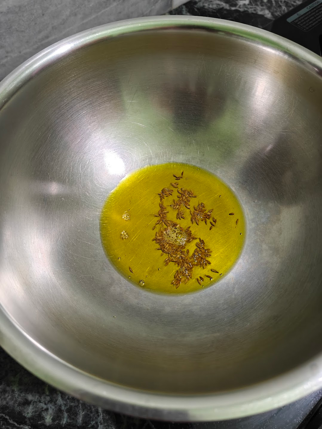 Cumin seeds being tempered in oil for paneer in white sauce.