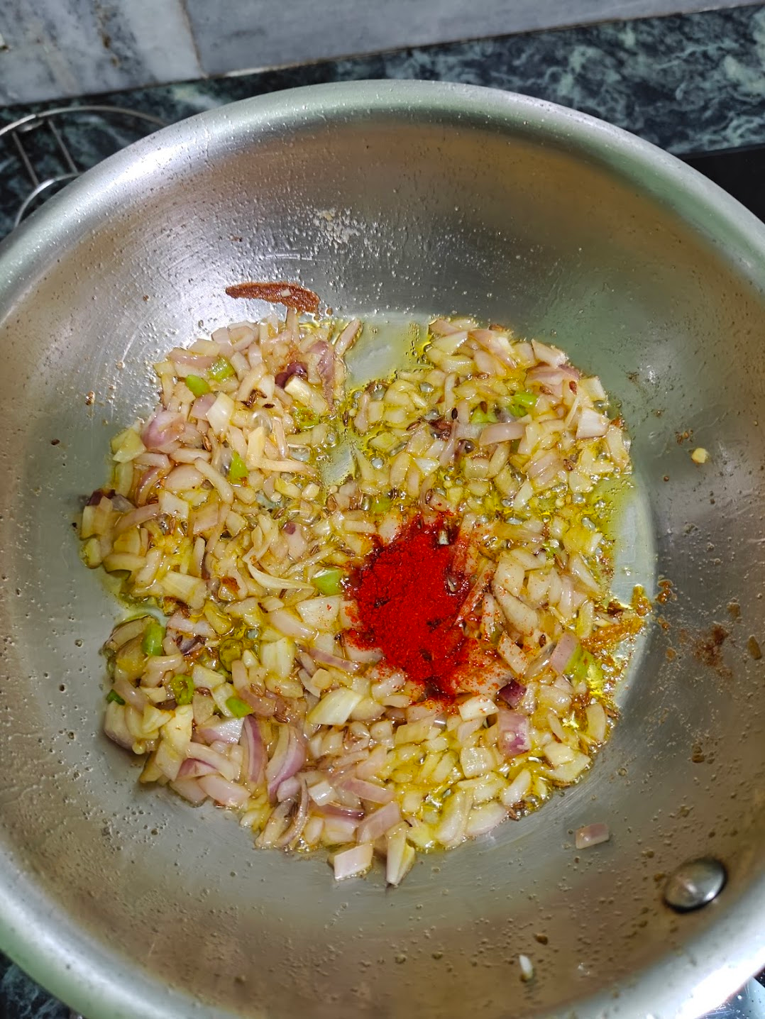 Adding the red chilli powder to the slightly cooked onions and chillies