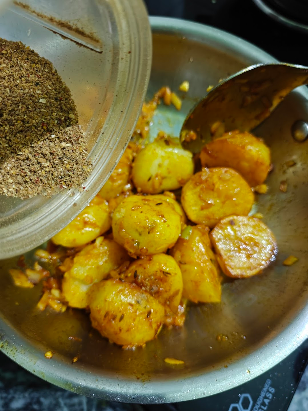 Adding ground achari masala over potatoes in a pan