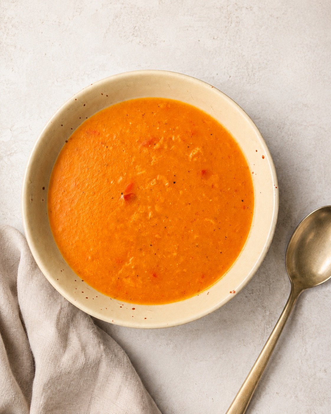Tangy mango soup served in a cream bowl with a spoon and cloth napkin
