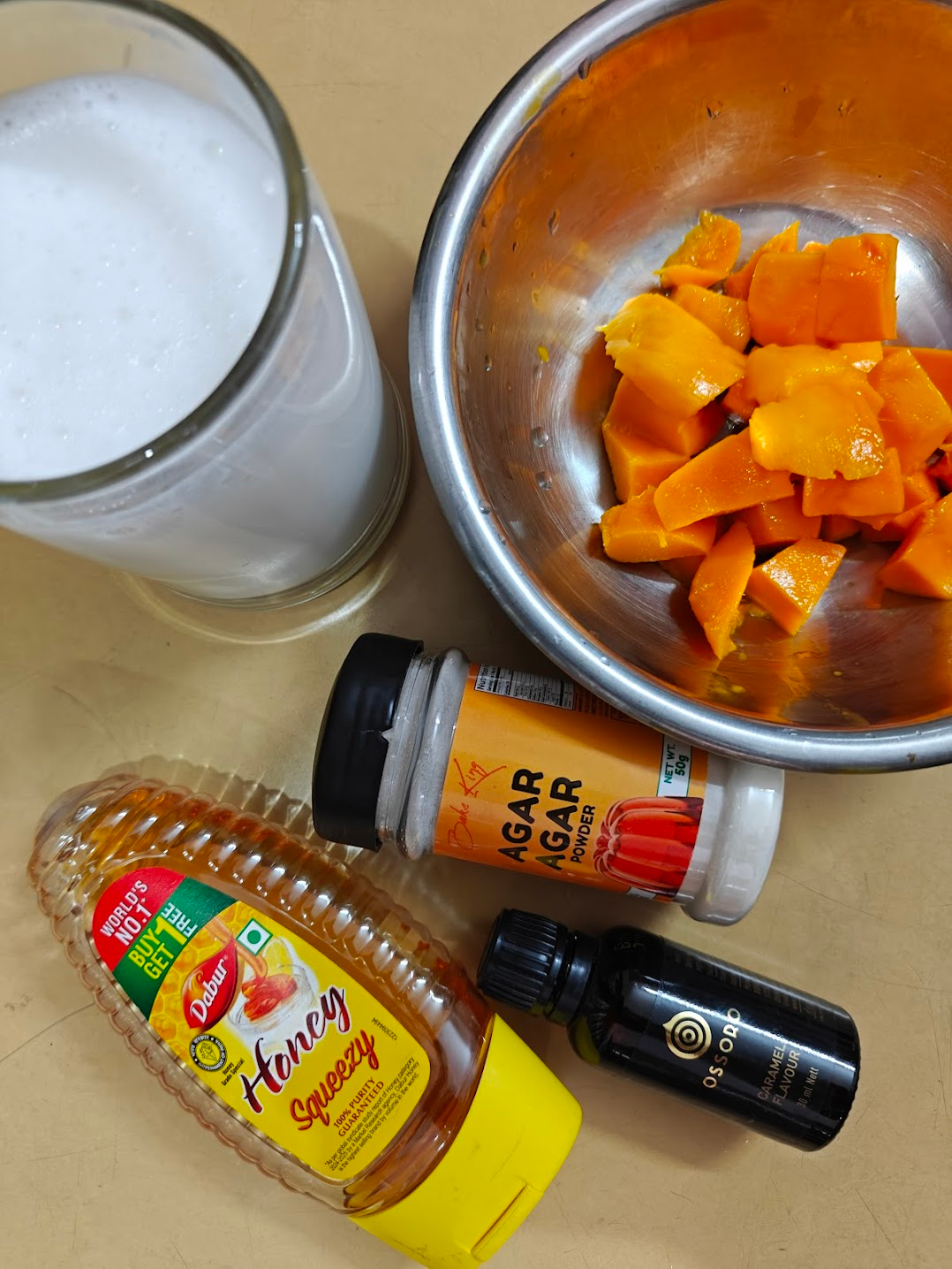 Ingredients for making mango pudding gathered together, including freshly cut mangoes, rich coconut milk in a cup, and a small container of agar agar powder, honey and caramel flavor. 