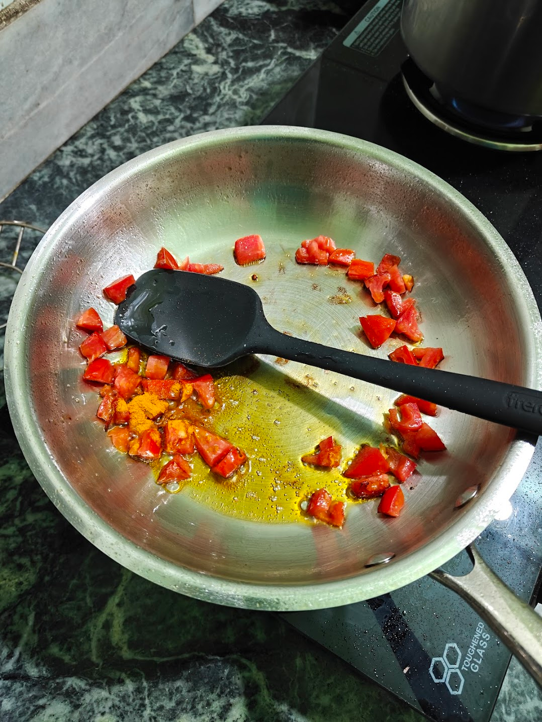 Turmeric powder added to softened tomatoes in a pan
