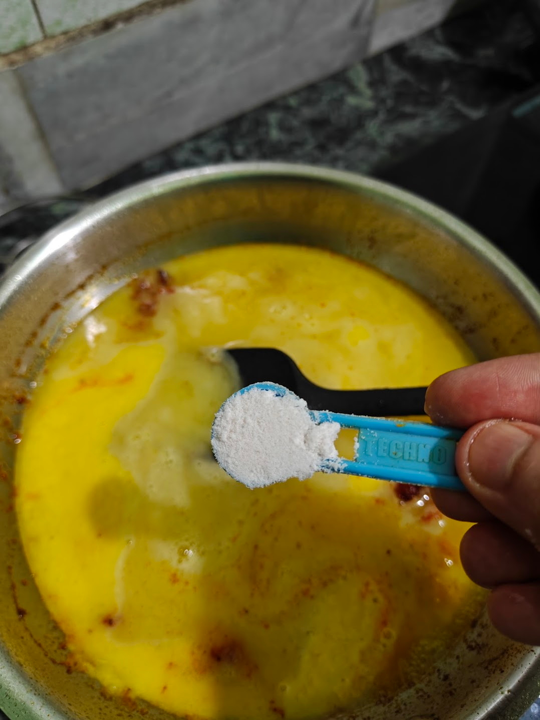 Salt being added to mango soup while it cooks in the pan