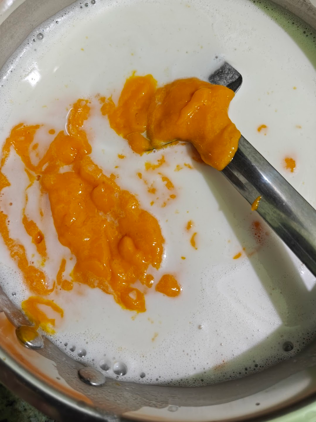Mango puree being stirred into the coconut milk mixture