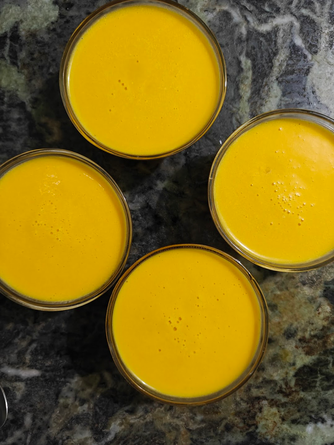 Four glass bowls filled with coconut mango pudding before chilling